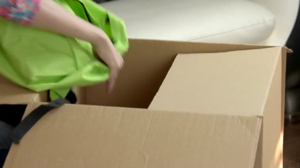 mains féminines emballant une boîte en carton boîte avec des vêtements - Séquence, vidéo