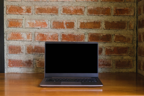 Computer portatile dello schermo vuoto sulla scrivania di legno e sfondo di mattoni rossi dietro. - Foto, immagini