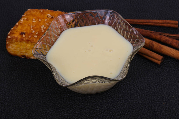 Kondenzované mléko v misce se sinnamonovými tyčinkami a pečivem - Fotografie, Obrázek