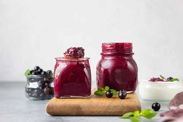 Jar of delicious homemade black currant curd, custard or jam with natural yogurt and fresh berries on grey concrete background. Healthy breakfast. - Foto, immagini