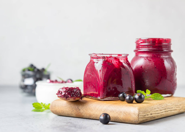 Jar of delicious homemade black currant curd, custard or jam with natural yogurt and fresh berries on grey concrete background. Healthy breakfast. - Foto, immagini