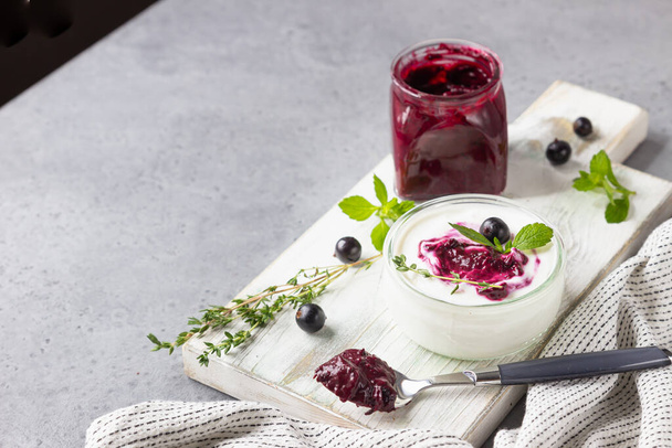 Jar of delicious homemade black currant curd, custard or jam with natural yogurt and fresh berries on grey concrete background. Healthy breakfast. - Zdjęcie, obraz