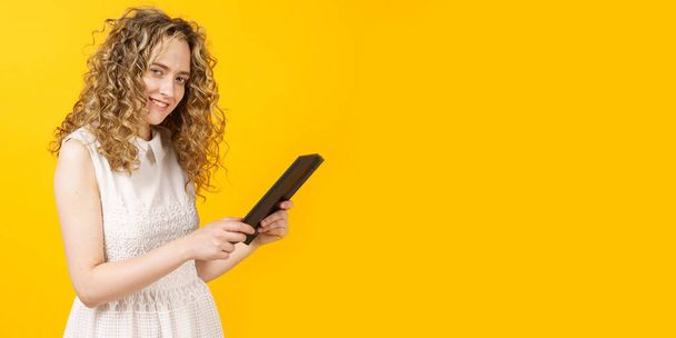 Portrait of a young woman who communicates on a tablet. Female portrait. Isolated on yellow background - Fotoğraf, Görsel