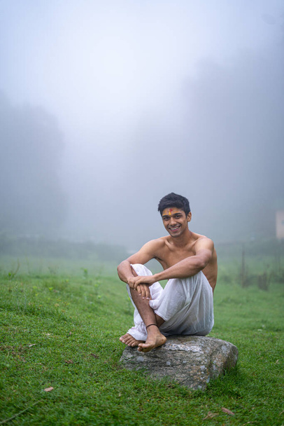 Fiatal jóképű ázsiai modell ül a hegyekben egy dhoti a reggel. - Fotó, kép