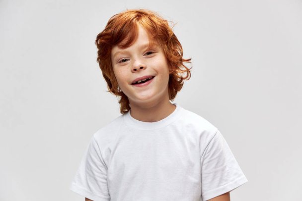 vöröshajú gyermek szórakoztató mosoly fehér póló vágott kilátás szürke háttér  - Fotó, kép