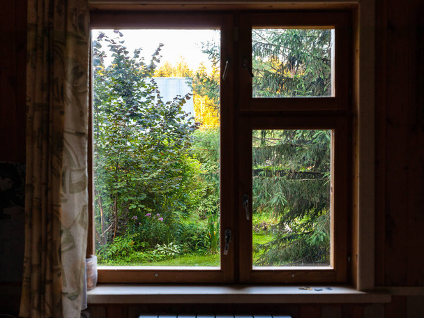θέα κατάφυτη αυλή μέσα από το παράθυρο του θερινού σπιτιού στο ηλιοβασίλεμα του καλοκαιριού - Φωτογραφία, εικόνα