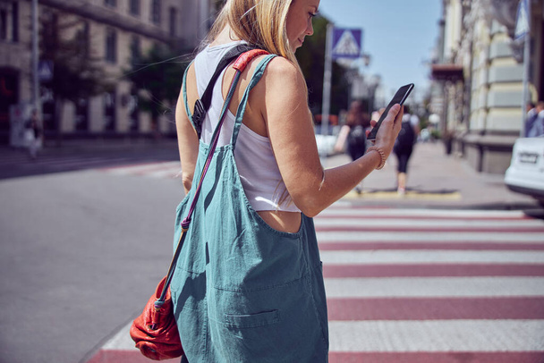 Menina de cabelos vermelhos com uma bolsa está lendo uma mensagem no smartphone
    - Foto, Imagem