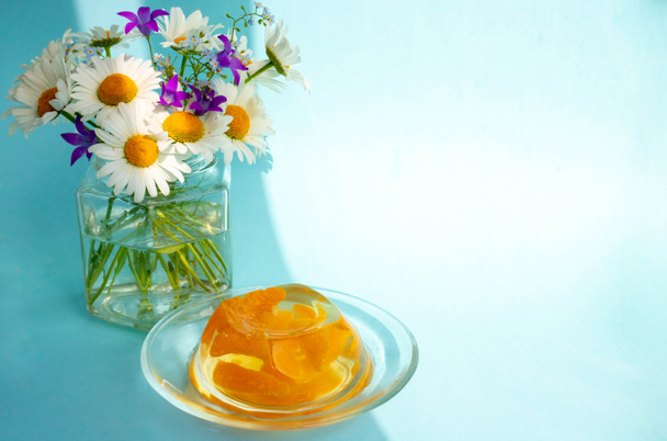 Jalea de desayuno con rodajas de mandarina y un montón de margaritas sobre un fondo azul - Foto, Imagen