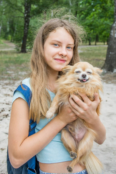 Op een heldere zomerdag in het bos houdt een meisje een hond in haar armen. Ze glimlachen.. - Foto, afbeelding