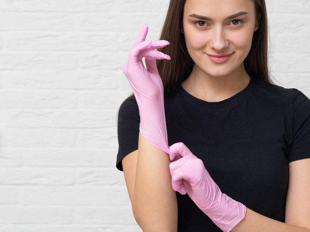 young woman cosmetologist and brow specialist puts on protective gloves and a mask to work with a client, - Photo, image