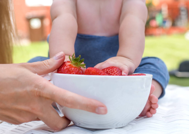 a child grabbing strawberries from a bowl - Фото, изображение