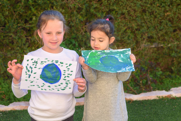 2人のかわいい女の子の肖像画が地球を描いています。子供たちは地球の絵を描く楽しい屋外. - 写真・画像