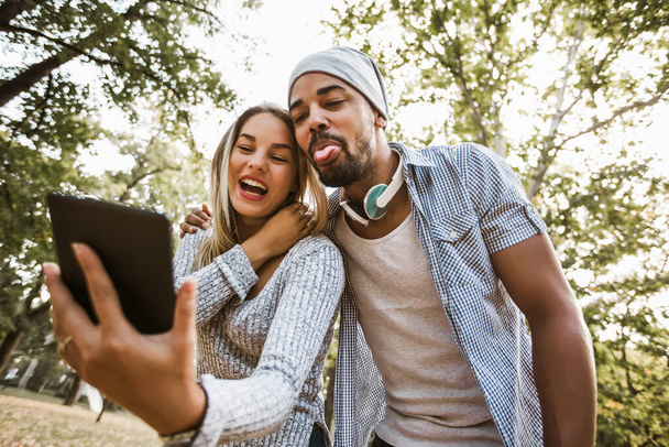 Outdoor portrait of romantic and happy mixed race young couple in park using digital tablet - Photo, Image