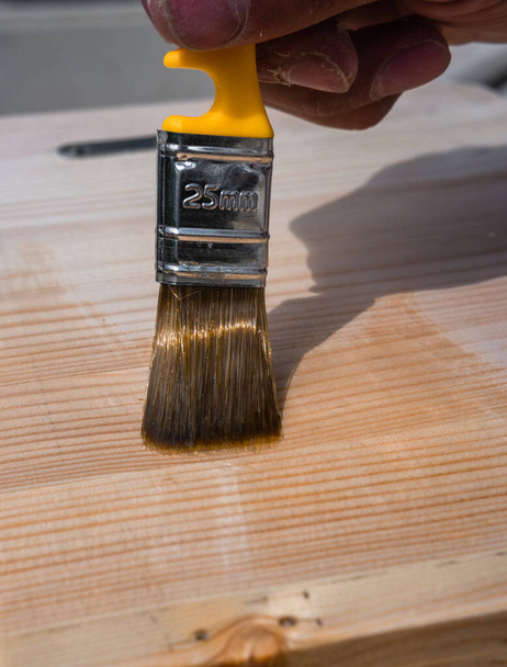 塗料ブラシを使用してニスで木を開きます。木製のテーブル、フェンス、または床にブラシ。ワニスで作業面を開きます。木の質感。木をニスで処理するには. - 写真・画像
