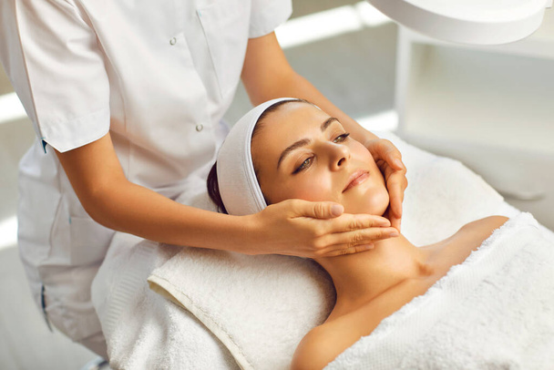 Spa facial massage. Beautician makes face massage to woman in white beauty salon - Fotó, kép