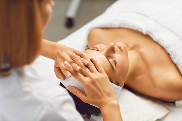 Facial skin beauty and health concept. A woman receives a facial massage from a clinic beautician - Foto, imagen