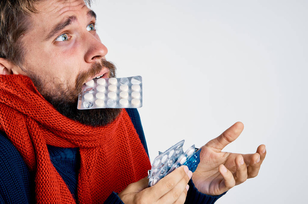 A man with pills in his teeth gestures with his hands health problems warm clothes red scarf - Photo, Image