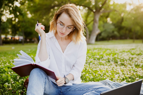 Young woman writing something in the notebook in the park. - Photo, Image
