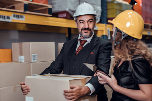 Inżynierka i biznesmen noszący twardy kapelusz stojący ładunek w magazynie towarowym i sprawdzający ładunek kontrolny ze statku towarowego Cargo do importu i eksportu. Koncepcja pracy zespołowej  - Zdjęcie, obraz