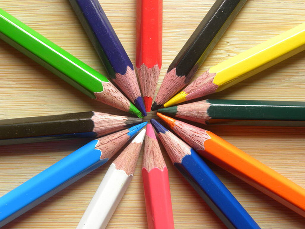 Muchos lápices de color dispuestos en círculo se mantienen en la mesa de madera - Foto, imagen