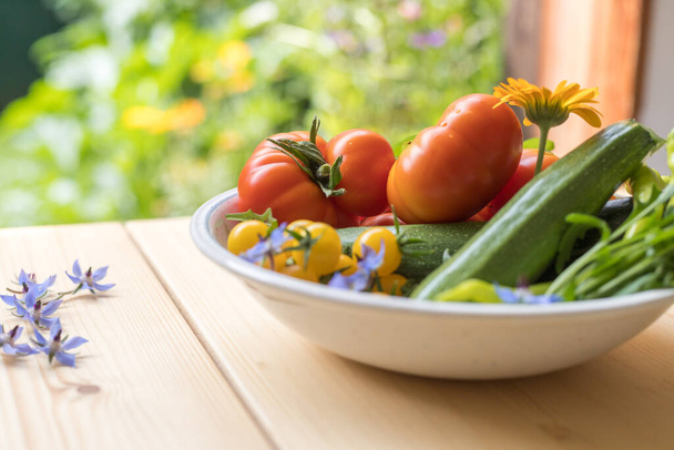Fresh colorful vegetables in a bowl, raised in the own garden. Tomatoes, zucchini, flowers and herbs. - Foto, Bild