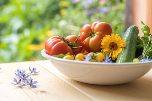 Fresh colorful vegetables in a bowl, raised in the own garden. Tomatoes, zucchini, flowers and herbs. - 写真・画像