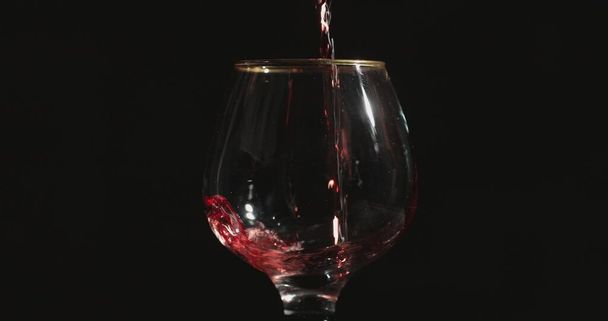 Pouring red wine into a glass, in front of black background - Foto, Imagen
