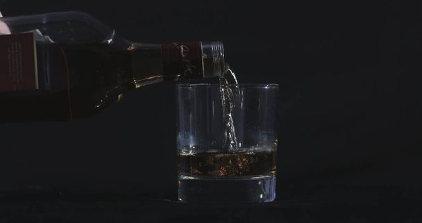 Fekete háttér előtt whiskyt öntenek egy pohárba. - Fotó, kép