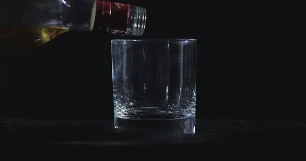 На фоне черного фона виски наливают в стакан. - Фото, изображение