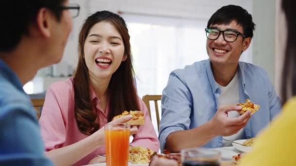 Joyeux groupe de jeunes amis déjeunant à la maison. Fête de famille en Asie manger de la pizza et rire en profitant du repas tout en étant assis à table ensemble à la maison. Vacances de célébration et convivialité. - Séquence, vidéo
