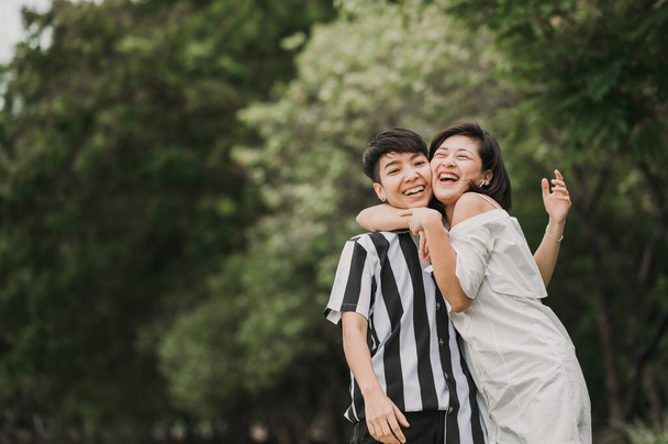 Mutlu Asyalı lezbiyen LGBT çifti parkta gülüp gülerken birbirlerine sarılıyorlar. - Fotoğraf, Görsel