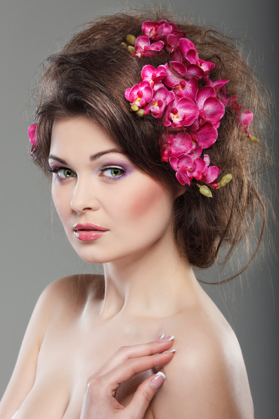 Portrait of beautiful sexual brunette with pink orchids in hairs. emotions, cosmetics - Фото, изображение