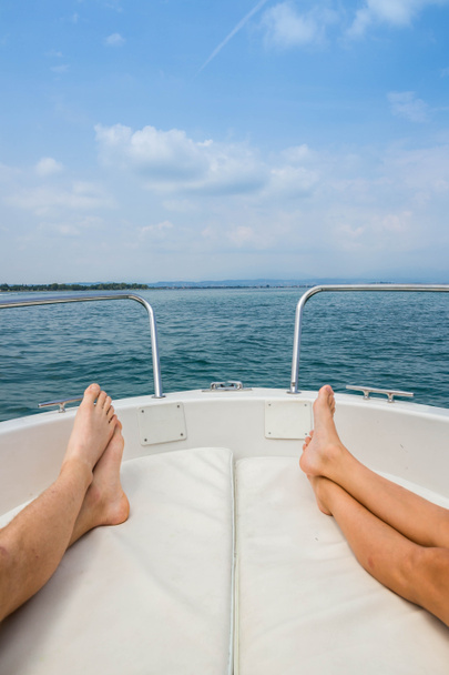 two pairs of feet, lake Garda, blue water, white boat, Italy, relaxing - Foto, afbeelding