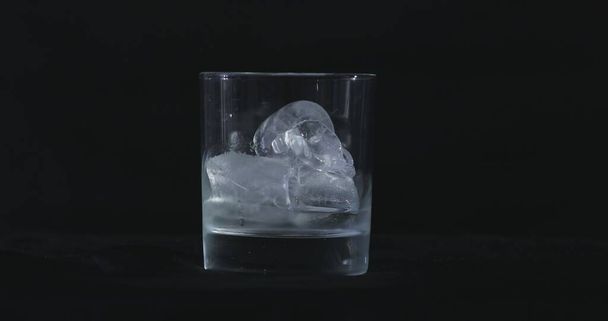 I cubetti di ghiaccio si sciolgono nell'alcol, il bicchiere di whisky e il fumo galleggia su uno sfondo nero - Foto, immagini