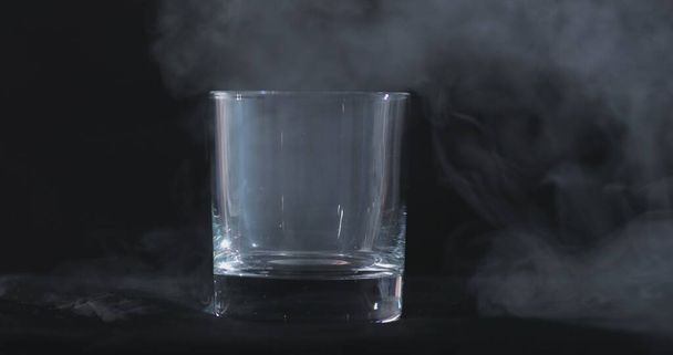 Boş bir viski, siyah bir arka planda alkol bardağı ve yüzen bir duman. - Fotoğraf, Görsel