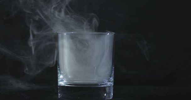 Un whisky vuoto, un bicchiere di alcol su uno sfondo nero e fumo galleggiante - Foto, immagini