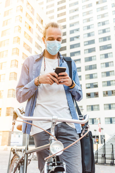 young tall young caucasian man with surgical mask and with vintage bike checking a phone - Photo, Image