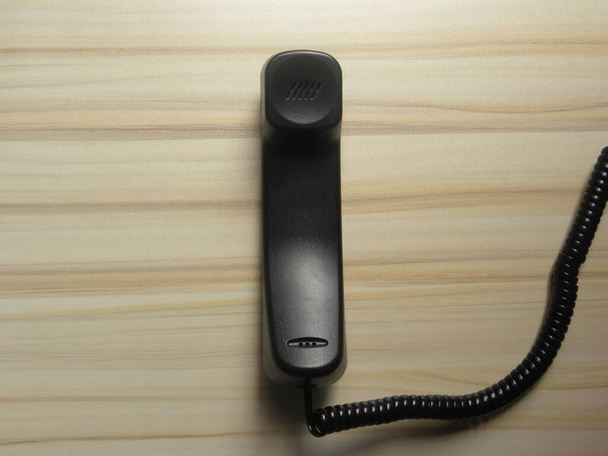 Черный приемник стационарного телефона хранится на деревянном столе - Фото, изображение