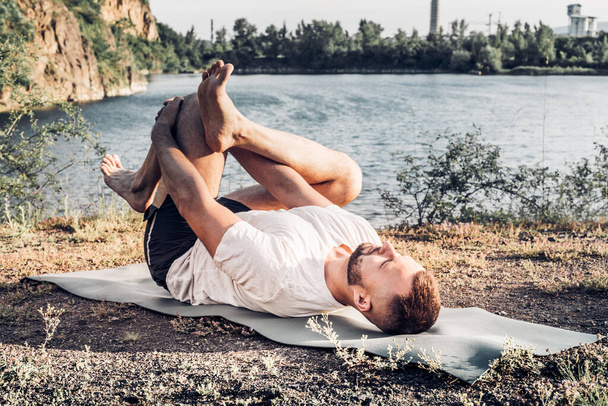 Jeune homme barbu qui fait du yoga tête baissée et debout asana. Beau fond paysage de lac de carrière de montagne. Complexe incroyable et drôle image de yoga. Journée internationale du Yoga - Photo, image