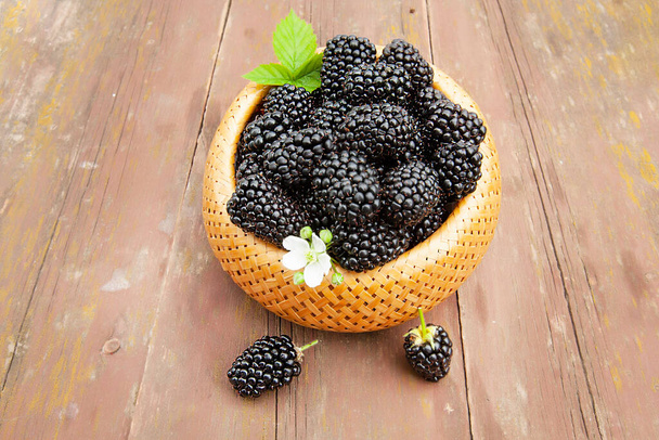 large ripe blackberries in a wicker basket on an old wooden table - Photo, Image