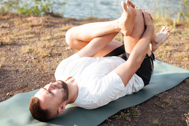 Young man doing yoga in morning park. Bearded man relax and streching in nature. International Day of Yoga - Foto, Bild