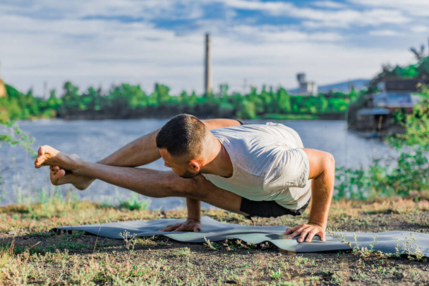 A young man sits on a quarry lake at sun, doing yoga. Sitting in yoga pose. Balance, harmony, concentration and relaxation. - Foto, Imagem