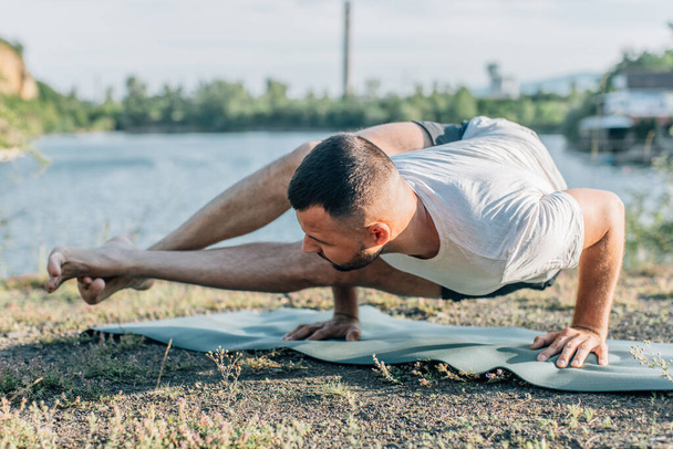 Un giovane uomo si siede su un lago di cava al sole, facendo yoga. Seduto in posa yoga. Equilibrio, armonia, concentrazione e relax. - Foto, immagini