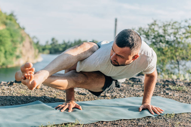 Morning and evening, a handsome young man doing yoga exercise on the shore of a quarry lake in nature in the summer outdoors. Healthy active lifestyle concept. - Photo, Image