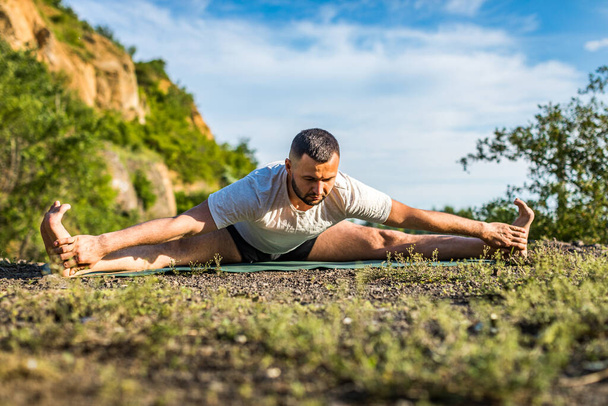 Homem fitness jovem fazendo exercício de ioga ao ar livre no lago pedreira. Jovem bonito com barba fazendo exercício de ioga
. - Foto, Imagem