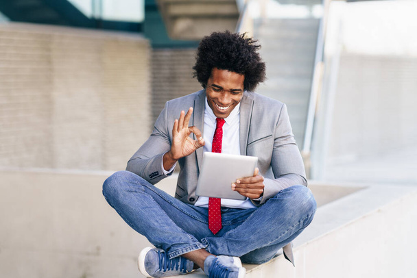 Černý podnikatel pomocí digitálního tabletu sedí v blízkosti kancelářské budovy. - Fotografie, Obrázek