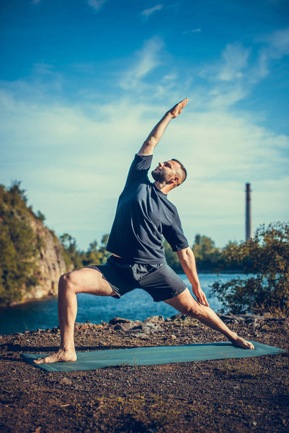 Man doing yoga exercise on the quarry lake at sunny day. International Day of Yoga. - 写真・画像