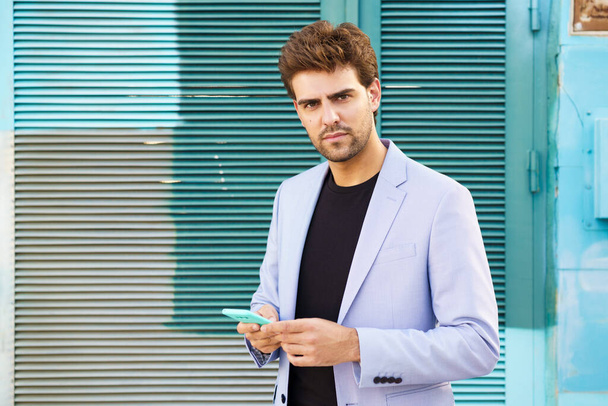 Fiatal üzletember kék öltönyt visel okostelefonnal városi háttérben. - Fotó, kép