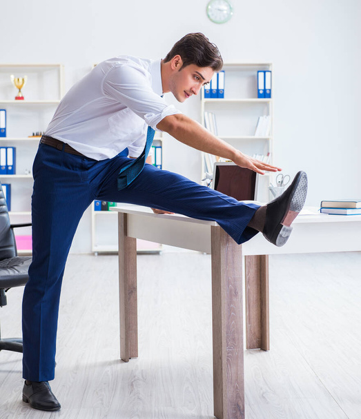 Young businessman doing sports stretching at workplace - Photo, Image