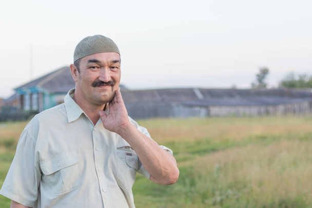 Muslimin vanhemman miehen muotokuva Siperian kylän taustalla, Venäjä - Valokuva, kuva